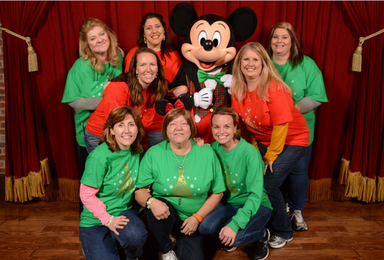 Group of girls wearing green and red t-shirts posing with a Mickey Mouse doll, capturing a fun and playful moment