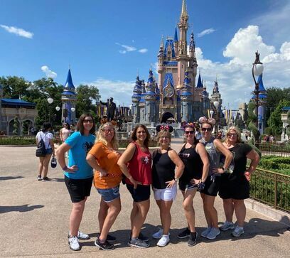 Group of girls wearing green and red t-shirts posing with a Mickey Mouse doll, capturing a fun and playful moment